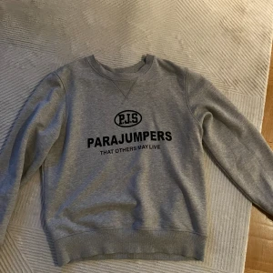 Grå sweatshirt från Parajumpers - Säljer en grå sweatshirt från Parajumpers i fleece. Den har en cool logga på bröstet och en patch på ärmen. Perfekt för kalla dagar och riktigt skön att ha på sig. Passar både till vardags och chillkvällar. 🖤