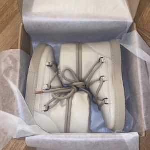 Beige moon boots i syntetmaterial Oanvända.  - Säljer ett par snygga beige moon boots i syntetmaterial. De är helt nya och perfekta för vintern. Skorna har en cool snörning framtill och är superbekväma att ha på sig. Perfekta för att hålla fötterna varma och stiliga under kalla dagar! Helt nya! 