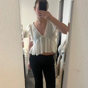 Vit blus med volanger - Säljer en superfin vit blus med volanger och v-ringning. Den är croppad och har en söt knytning i ryggen. Blusen är i mycket bra skick och är ifrån Zara.