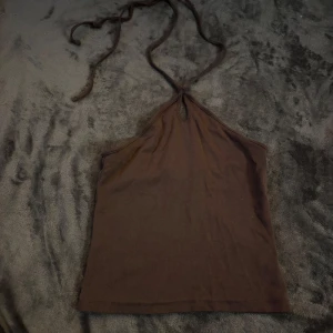 Brun halterneck topp från BikBok - Säljer en snygg brun halterneck topp från BikBok i storlek XS. Perfekt för sommardagar eller en kväll ute. Toppen är i ett mjukt material och har en enkel design som gör den lätt att matcha med olika outfits.