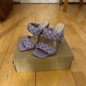 Lila klackskor från Steve Madden - Snygga lila klackskor från Steve Madden med flätade remmar och öppen tå. Helt oanvända. Storlek 38.