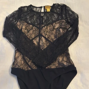 Svart spetsbody från h&m - Elegant svart spetsbody från h&m med långärmad design och transparent spetsdetaljer. Perfekt för en stilfull look med en feminin touch. Stängs med knappar i ryggen.