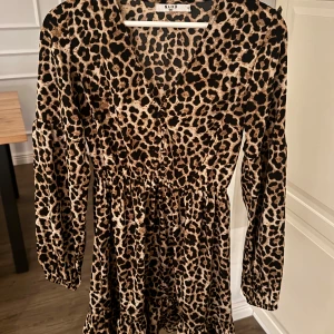 Leopardmönstrad klänning från NA-KD -  leopardmönstrad klänning från NA-KD med v-ringning och långa ärmar och volang nedtill