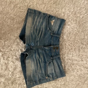 Lågmidjade blå jeansshorts från Black Bat  - Snygga blå jeansshorts från Black Bat med coola detaljer som dubbla knappar och fickor med mönstrad insida. Perfekta för en avslappnad stil. Dom är väldigt lågmijade. Storlek 36/27. Aldrig använda. Skriv för frågor och fler bilder.