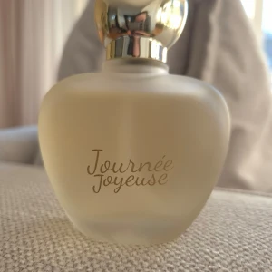 Journée Joyeuse Eau de Parfum - Elegant flaska med rundad form och gyllene kork. Parfymen Journée Joyeuse har en volym på 100 ml. Perfekt för den som söker en sofistikerad doftupplevelse. Säljs utan förpackning. 