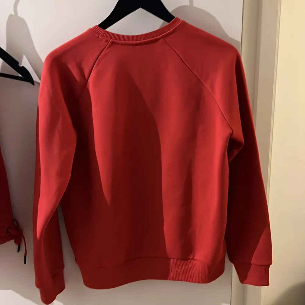 Säljer en snygg röd sweatshirt från Peak Performance med broderad logga på framsidan. Tröjan har långa ärmar och ribbade muddar vid ärmslut och nederkant. Perfekt för en avslappnad stil.. Neuletakit & Villapaidat.