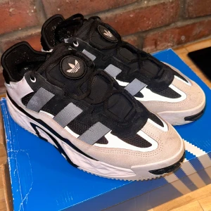 Adidas sneakers i svart och vit  - Snygga Adidas sneakers i svart och vit med silvriga detaljer. Skorna har en modern design med svarta och gråa inslag samt den klassiska Adidas-loggan. Perfekta för en sportig look. Knappt använda.