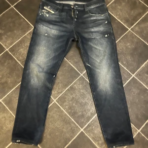 Mörkblå jeans från Diesel - Snygga mörkblå jeans från Diesel med slitna detaljer och en klassisk femficksdesign. Jeansen har en dragkedja och knapp framtill samt en liten logotyp på fickan. Jeansen är helt nya i storlek 34/32 men upplagda så skulle säga numera en 34/30. Nypris är 2000kr, mitt pris är 800kr