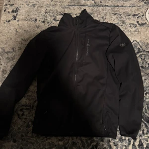 Svart softshelljacka från Sail Racing - Säljer en svart softshelljacka från Sail Racing. Jackan har en stilren design med dragkedja framtill och är tillverkad i polyester. Perfekt för svala dagar. Pris kan snackas