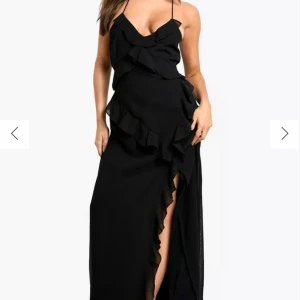 Svart långklänning/balklänning med volangdetaljer - Elegant svart långklänning med smala axelband och volangdetaljer längs framsidan. Den är endast använd en gång!  Har inga dekaler