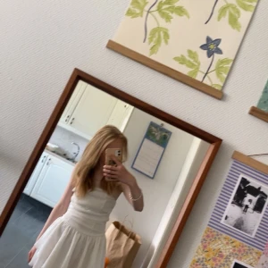 Vit axelbandslös klänning - Säljer en söt vit axelbandslös klänning med volanger. Klänningen har en smockad överdel och en luftig kjol med lager. Perfekt för sommarens alla tillfällen!