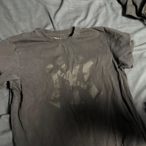 Svart t-shirt från '47 - Säljer en svart t-shirt från '47 med ett stort tryck av en logotyp på framsidan. T-shirten är kortärmad och har en klassisk rund halsringning. Perfekt för en avslappnad stil.