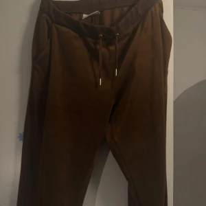 Bruna mjukisbyxor från Juicy Couture - Snygga bruna mjukisbyxor från Juicy Couture med snörning i midjan. Perfekta för en avslappnad stil. Tillverkade i ett mjukt material som ger en bekväm passform.