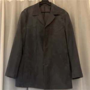 Grå rock från Batistini - Elegant grå rock från Batistini med klassisk design och knappar framtill. Perfekt för kyligare dagar med sin stilrena look.