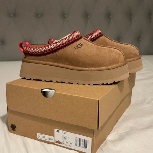 Uggs tazz slipper chestnut  - Jag säljer mina Uggs tazz slippers st 36 i färgen chestnut som har en röd kant. Fick dessa i julklapp och de är helt nya ur kartongen och alltså i ett helt perfekt skick! Säljer pga att det blev fel storlek! ❤️🍁(❗️!! Tryck inte på köp direkt, skriv först!! ❗️)