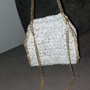 Vit/grå spräcklig virkad väska med guldkedja - Snygg vit/grå spräcklig virkad väska med en glittrig guldkedja. Perfekt för att ge en touch av glamour till din outfit. Väskan har en unik textur och är både stilren och trendig.