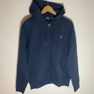 Ralph Lauren zip-up hoodie - FÖRSTA TILL 750kr ELLER HÖGSTA ERBJUDANDET INNAN LÖRDAG VINNER!	✅•	Marinblå Ralph Lauren zip-up hoodie 	•	Storlek: M 	•	Klassisk design med broderad logotyp på bröstet 	•	Dragkedja framtill och justerbar huva 	•	I mycket bra skick!