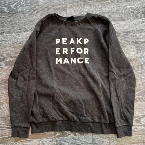 Mörkgrå tröja från Peak Performance - Snygg mörkgrå tröja från Peak Performance med vit text på framsidan. Perfekt för en avslappnad stil. Tröjan har långa ärmar och en bekväm passform. Tröjan passar bra på mig som är 170 cm och den är i ett fint skick