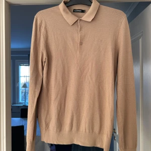 Beige pikétröja från J.Lindeberg - Snygg beige pikétröja från J.Lindeberg med klassisk krage och knappar framtill. Tröjan har långa ärmar och en stilren design som passar perfekt för en avslappnad men ändå uppklädd look. 300kr