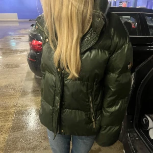 Grön pufferjacka med dragkedja - As snygg grön pufferjacka från Michael kors med dragkedja och hög krage. Perfekt för kyliga dagar !! Köpt för 5500 och säljer för 200. INGA defekter alls, som ny då jag bodde utomlands när jag köpte denna och inte hade någon använding av den🌸🩷