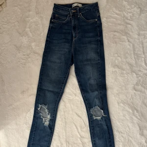 Jeans med slitningar - Jeans i modellen Gina från Ginatricot. Alla hål och slitningar är enligt modellen, inte själv gjorda. Använda enstaka gånger och är i mycket bra skick utan inga vidare tecken på användning. Stretchiga i storlek 34