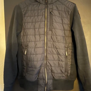 Svart quiltad jacka med huva - Snygg svart jacka med quiltade detaljer och huva från PJS. Jackan har dragkedja framtill och praktiska fickor med dragkedja. Storlek är Y/L och det står för youth large storlek. Det är 38 barn storlek 