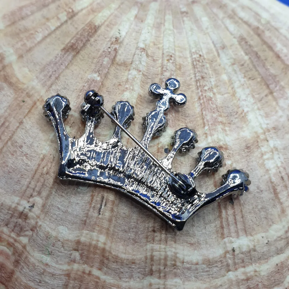 En brosch föreställande en krona, storlek ca 5x3cm. Svartmetallic/Gunmetalpläterad metall med vacker ytstruktur och kristaller I flera färger. . Asusteet.
