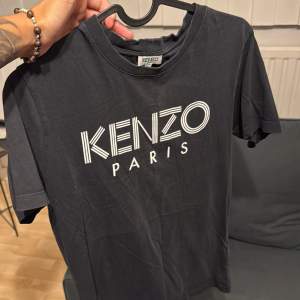 Säljer en snygg svart t-shirt från Kenzo i storlek XS. Den har en cool logga på framsidan med texten 'KENZO PARIS'. Passar perfekt för både vardag och fest!