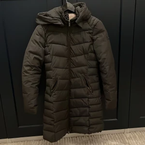 Livelo lång jacka - En lång och varm jacka från Livelo i storlek 34, passar mig som brukar ha XS/32. Lång ner till knäna (157cm) och värmer bra, finns dessvärre ingen päls till luvan! 