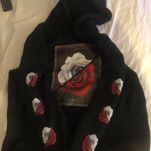 Svart Hoodie - En svart hoodie med rosor som tryck både på armarna och bröstet. Storlek XL väldigt skönt material. Inte så andvänd och i bra skick. Köparen står för frakten.