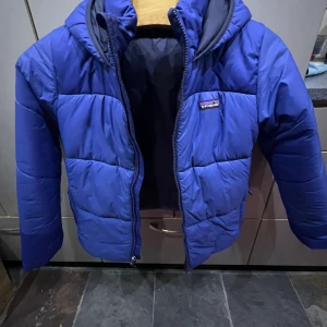 Vinterjacka 10-12Y Patagonia Blå - Fin täckjacka för 10-12 åring. Mellanblå och varm (vinterjacka). Inköpt på NK och  min son har använt den sparsamt under en säsong. Inte jättestor i storleken, mer för 10-11 åring även om det står 12 år. 