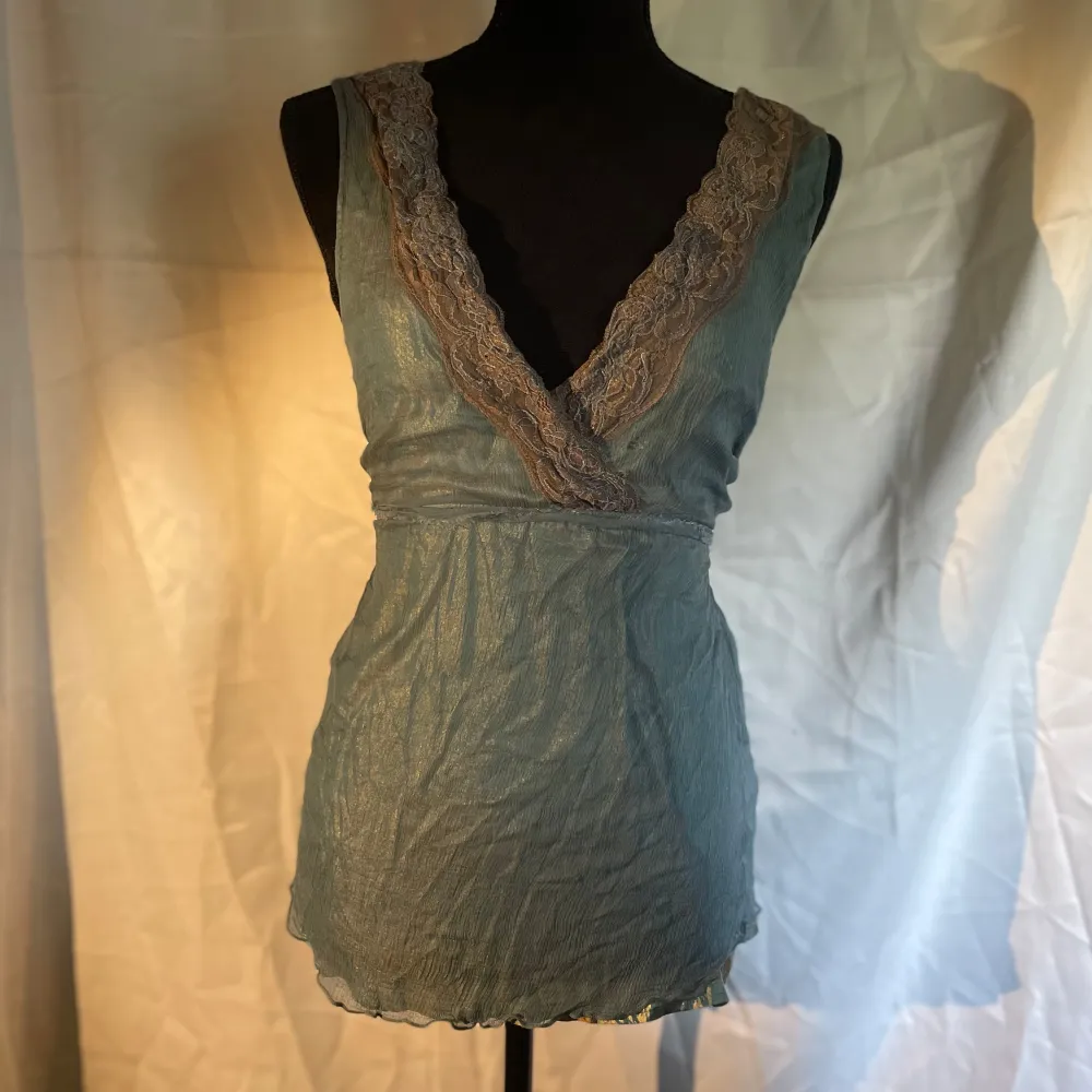 Ett vackert blått över tyg på en skimrande blå/guldigt tyg med en brun lace. Väldigt vackert linne med stor öppning för framme. Du kan välja att knyta där bak med tråden eller ha det löst. Väldigt skön att ha på sig . Yläosat.