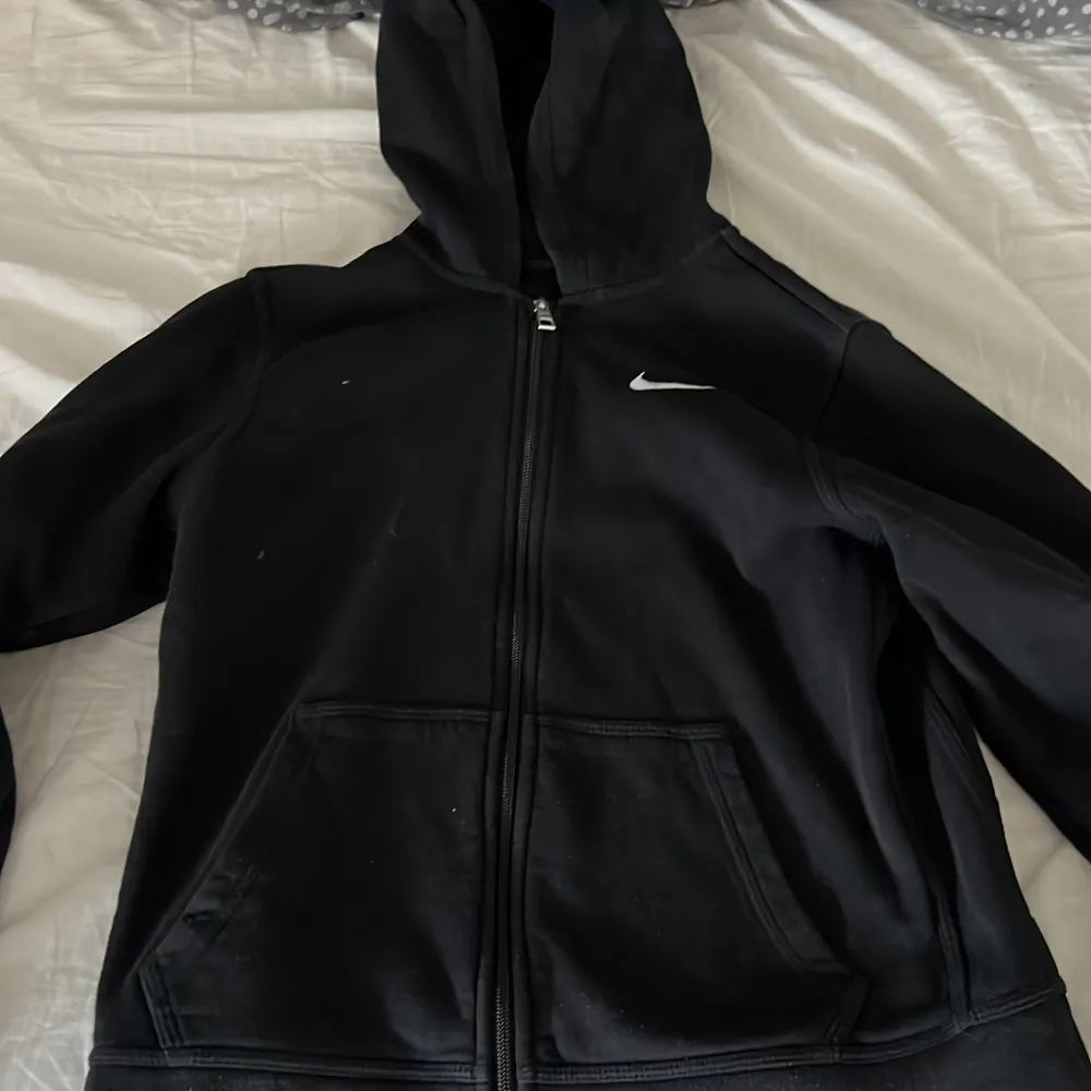 Säljer en svart hoodie från Nike med dragkedja och huva. Den har en klassisk design med en liten vit Nike-logga på bröstet. Perfekt för vardagsbruk eller träning.. Jackor.