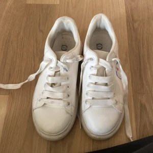 Vita sneakers med Doraemon-motiv - Säljer ett par vita sneakers i storlek 37 med ett coolt Doraemon-motiv på sidan. Skorna har snörning och är i syntetmaterial. Perfekta för en avslappnad och lekfull stil!