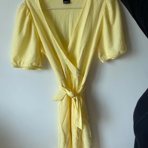 Gul omlottklänning från Gina Tricot - Säljer en superfin gul omlottklänning från Gina Tricot. Den har korta ärmar och ett knytband i midjan som ger en snygg passform. Perfekt för sommardagar eller en festlig kväll! 💛