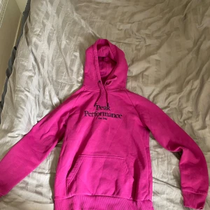 Rosa hoodie från Peak Performance - Säljer en snygg och bekväm rosa hoodie från Peak Performance. Den har en klassisk design med en stor ficka fram och justerbar huva. Perfekt för både vardag och chill. Peak Performance-loggan är broderad på framsidan. Passar perfekt för höst och vår!
