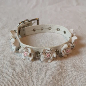Vit armband med rosor och nitar - Söt blommig choker med nitar på. Använt skick. Finns lite gråaktiga skador på några av rosorna som inte är märkbara på avstånd (se bild nr 2). ***Köpare står för frakt om inget annat anges