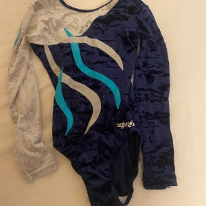Långärmad gymnastikdräkt  - Långärmad gymnastik dräkt i färgerna marinblå, silver/grå med turkosa detaljer. Den är knappt använd men har några trådar som sticker ut! Det står ingen storlek men skulle säga att den passar barn mellan 6-11år