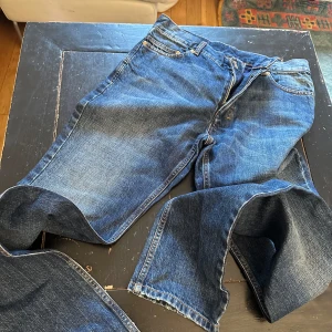 Blå jeans från Yves Saint Laurent - Säljer ett par snygga blå jeans från Yves Saint Laurent. De har en klassisk femficksdesign med märkets ikoniska logga broderad på bakfickan. Jeansen har en knapp med texten 'Yves Saint Laurent' och är i ett slitstarkt denimtyg. Perfekta för både vardag och fest!