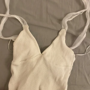 Vit ribbad klänning från Zara - Säljer en superfin vit ribbad ktopp från Zara. Den har smala axelband och en stilren design som passar perfekt till sommaren. toppen är i nyskick och redo för fest eller en dag på stan!