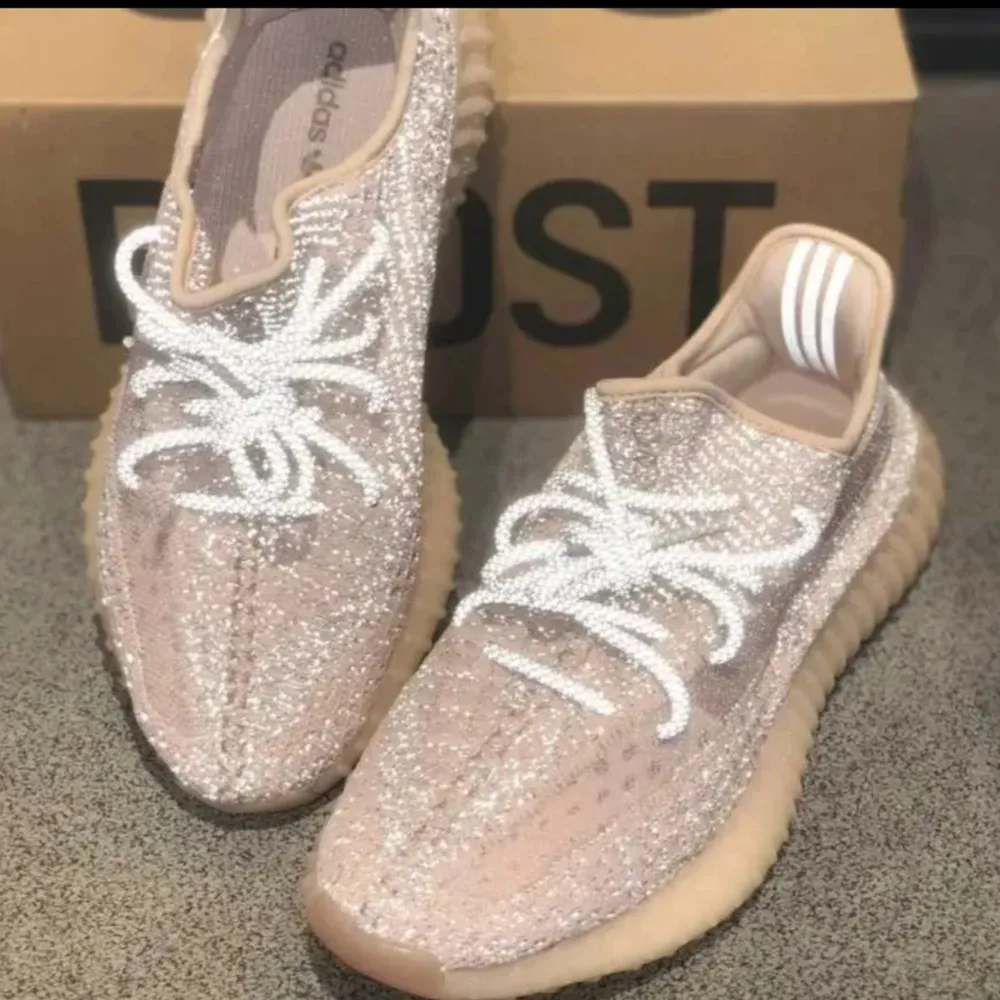 Säljer ett par snygga Adidas Yeezy Boost 350 V2 i en stilren beige färg. Skorna har en glittrig yta med vita snören och en bekväm, ribbad sula. Perfekta för både vardag och fest!. Skor.