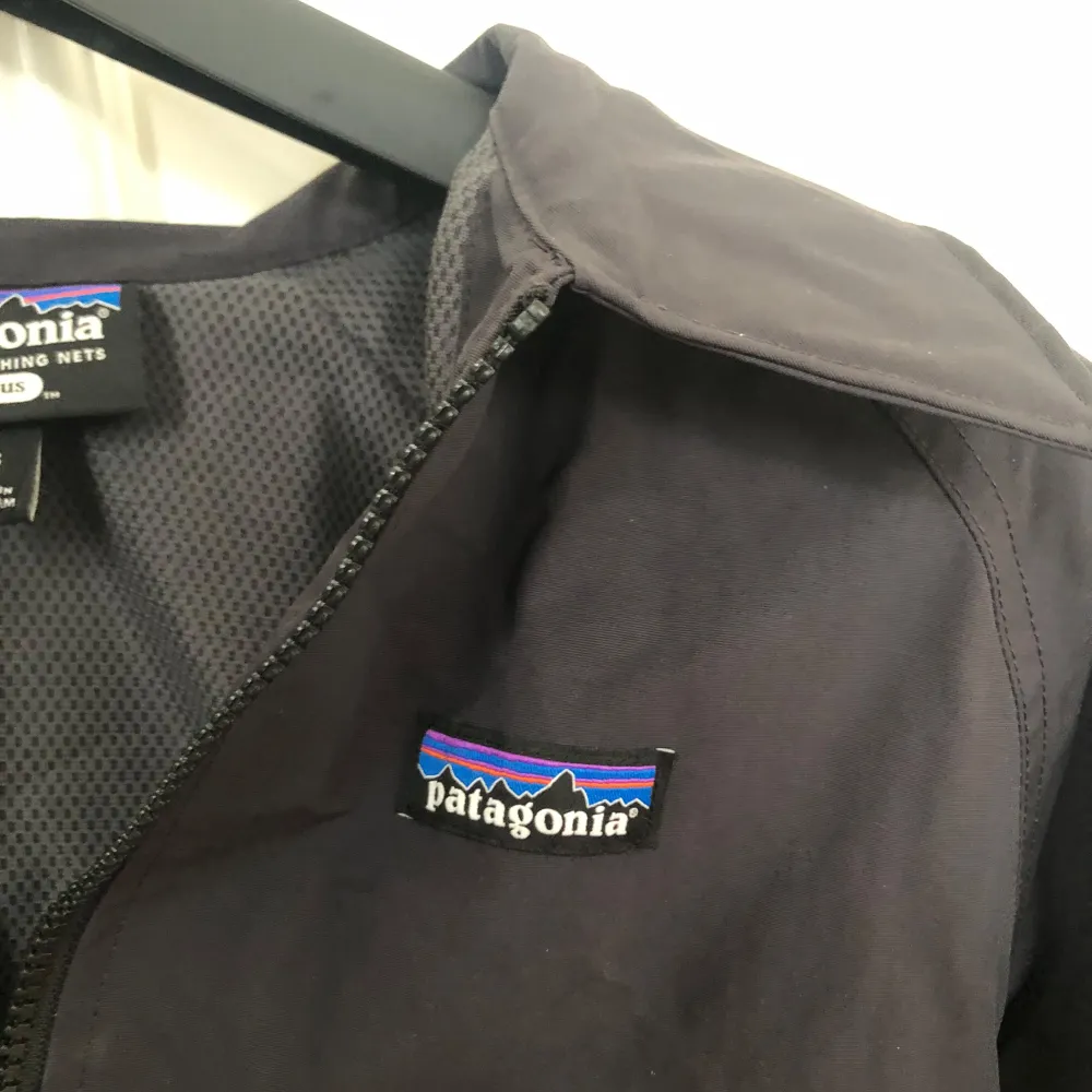 Säljer en stilren svart vindjacka från Patagonia, tillverkad av återvunna fiskenät. Jackan har dragkedja framtill och två praktiska fickor med dragkedjor. Perfekt för blåsiga dagar och lätt att packa med sig. Nypris: 2599kr. Skick: 10-10. Takit.