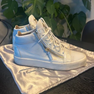 Vita Giuseppe Zannotis  - Snygga vita sneakers från Giuseppe Zanotti med dragkedja och snörning. Skorna har en högre modell med en platt sula och är tillverkade i skinn. Perfekta för en stilren look. Nypris ligger på ca 7-8 tusen. Dustbag medföljer.