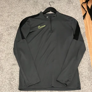 Grå långärmad tröja från Nike. ord pris 650kr - Säljer en grå långärmad tröja från Nike med Dri-FIT-teknologi. Tröjan har en dragkedja vid halsen och svarta detaljer på axlarna. Perfekt för träning eller vardagsbruk.