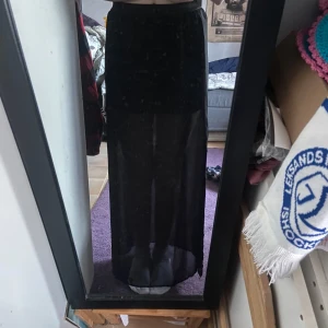 Svart långkjol från H&M Divided - Snygg svart långkjol från H&M Divided med transparenta detaljer. Kjolen har en elastisk midja och en slits på sidan. Använd ett par gånger och har små defekter som man inte tänker på, säljer då den inte kommer till användning längre🌸