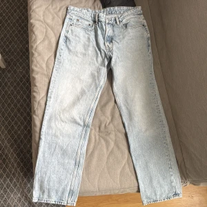 Ljusblå jeansbyxor - Säljer ett par ljusblå jeansbyxor med klassisk femficksdesign och knappgylf. De har en straight passform och är perfekta för en avslappnad stil. Passar bra till både sneakers och kängor. Storlek EUR 42