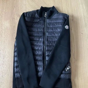Svart cardigan jacka från Moncler - Säljer en stilren svart cardigan jacka från Moncler med dragkedja framtill. Jackan har långa ärmar och ribbade muddar. Perfekt för kyligare dagar med sin snygga och funktionella design. Dragkedjan kan strula ibland men inga större problem. Pris kan diskuteras. Stl M passar 175-185.