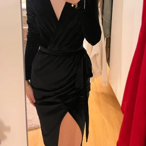 Svart omlottklänning från NLY Trend - Snygg svart omlottklänning från NLY Trend i storlek XS. Klänningen har en v-ringad design med långa ärmar och en elegant slits framtill. Perfekt för en stilren look med ett knytband i midjan som ger en fin passform.