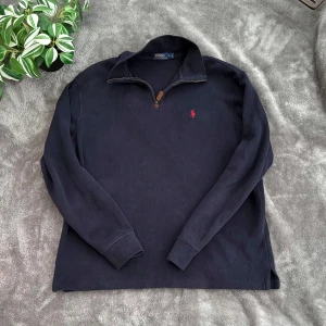 Blå 1/4 Zip från Ralph Lauren - Säljer en stilren mörkblå 1/4 zip från Ralph Lauren med dragkedja och röd broderad logga på bröstet. Perfekt för en avslappnad och snygg look. Tröjan har långa ärmar och en klassisk krage. 📦skickas med PostNord.