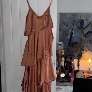 Skitsnygg orange långklänning  - Snygg mörkorange klänning med axelband och volangdetaljer. Tillverkad i ett glansigt material som ger en lyxig känsla. Perfekt för en elegant kväll. Funkar som både balklänning och sommarklänning. 